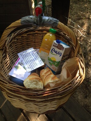 A wicker basket containing a juice carton, a loaf of bread, and a plastic bag. - Vrbo Property (Cléville)