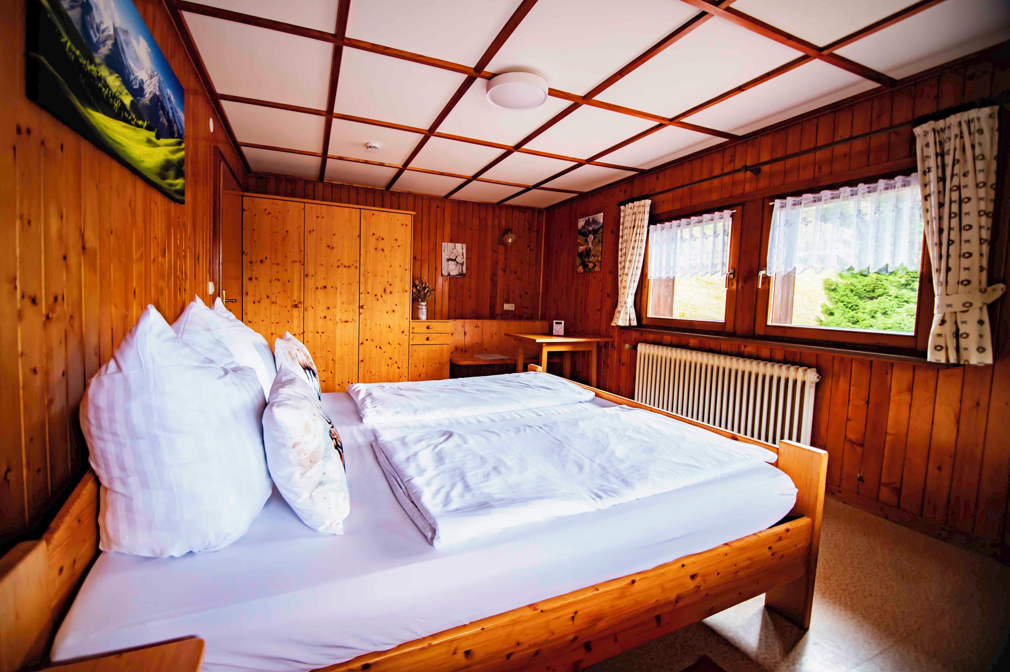 Una habitación de cabaña de madera con una cama, una ventana con cortinas y un radiador.