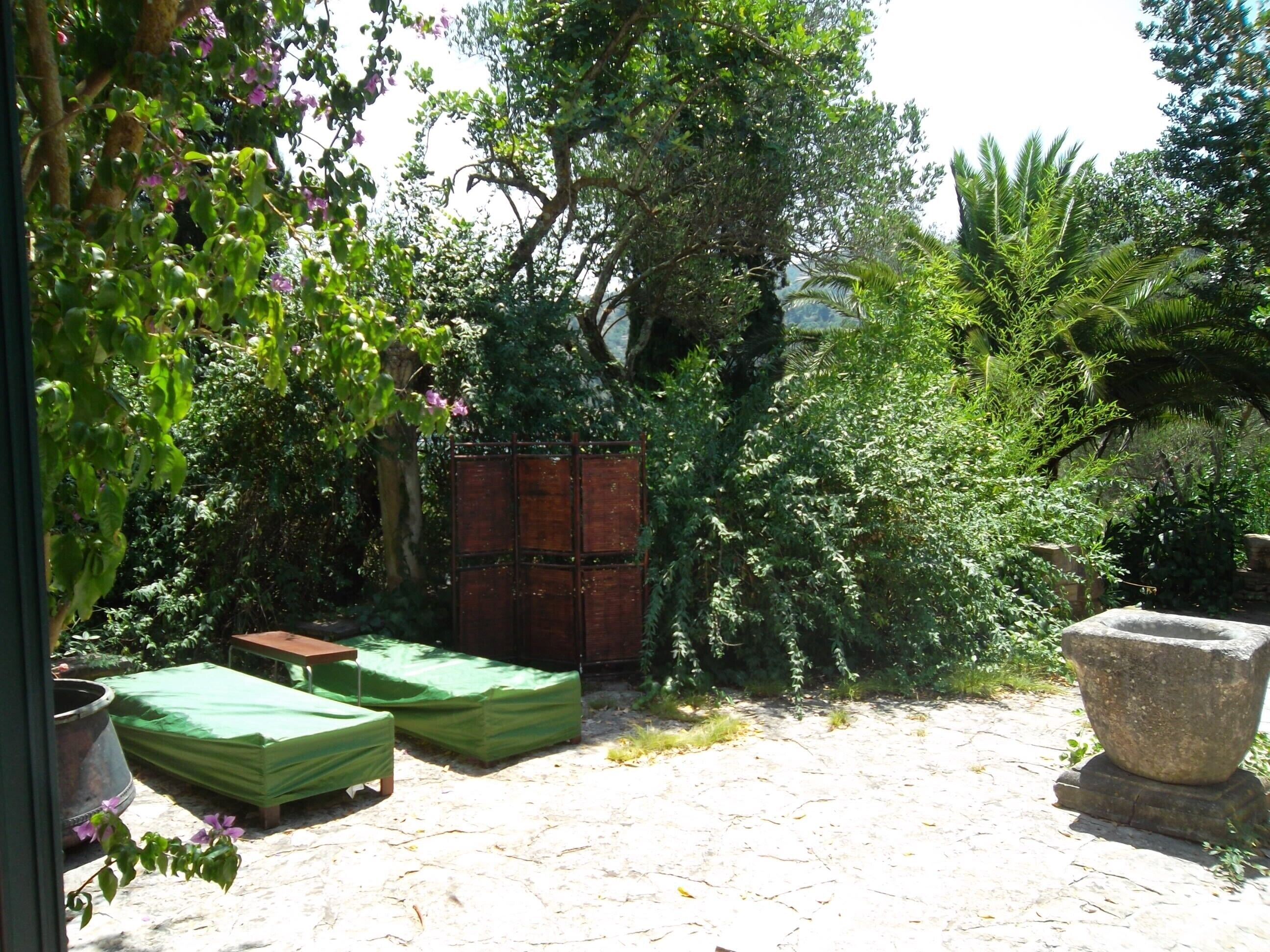 A garden with a wooden fence, a stone planter, and covered furniture.