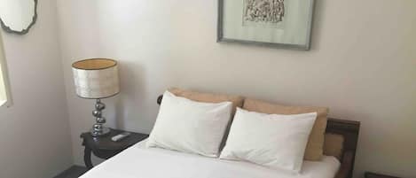 A neatly made bed with white linens, a bedside lamp, and a framed picture on the wall.
