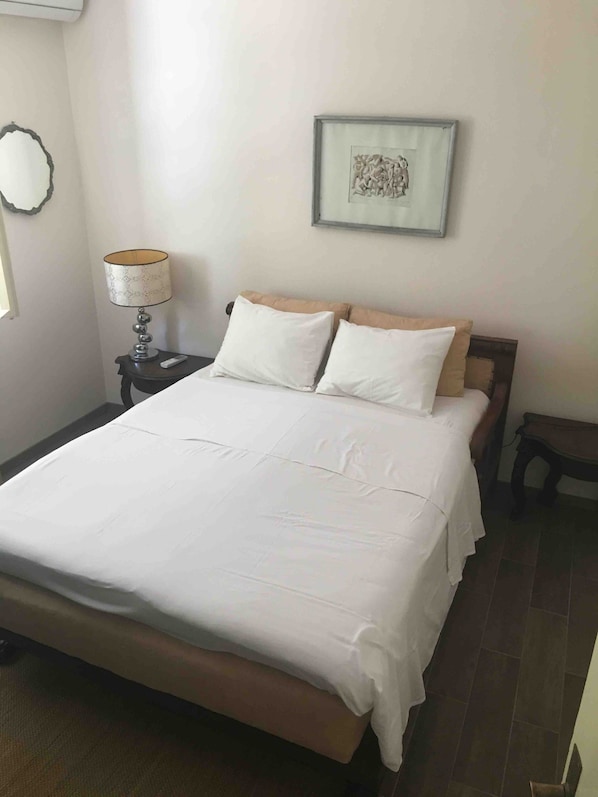 A neatly made bed with white linens, a bedside lamp, and a framed picture on the wall.