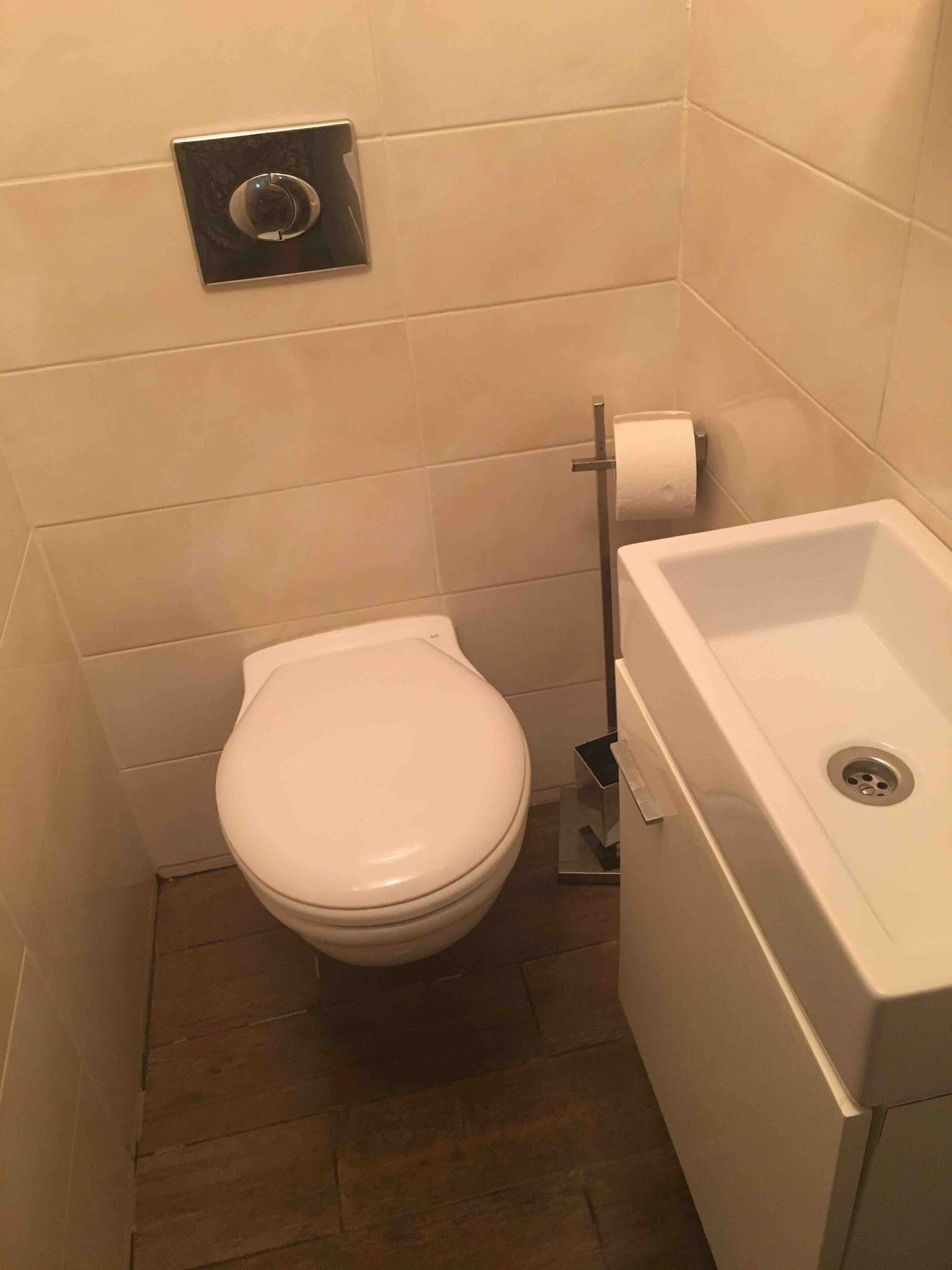 Ein kleines Badezimmer mit Toilette, Waschbecken und Toilettenpapierhalter.