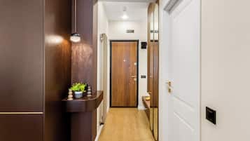 A hallway with a wooden floor, a plant on a shelf, and a door with a mirror.