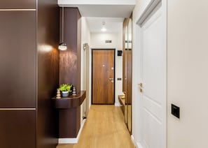 Um corredor com piso de madeira, uma planta numa estante e uma porta com espelho.