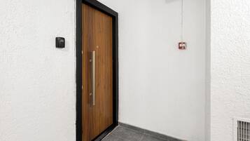 A door with a vertical handle and a black frame, set in a hallway with white walls and grey tiled flooring.
