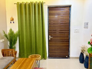 Una habitación con puerta de madera, cortina verde, una mesa de madera, un banco de madera y una planta en maceta.