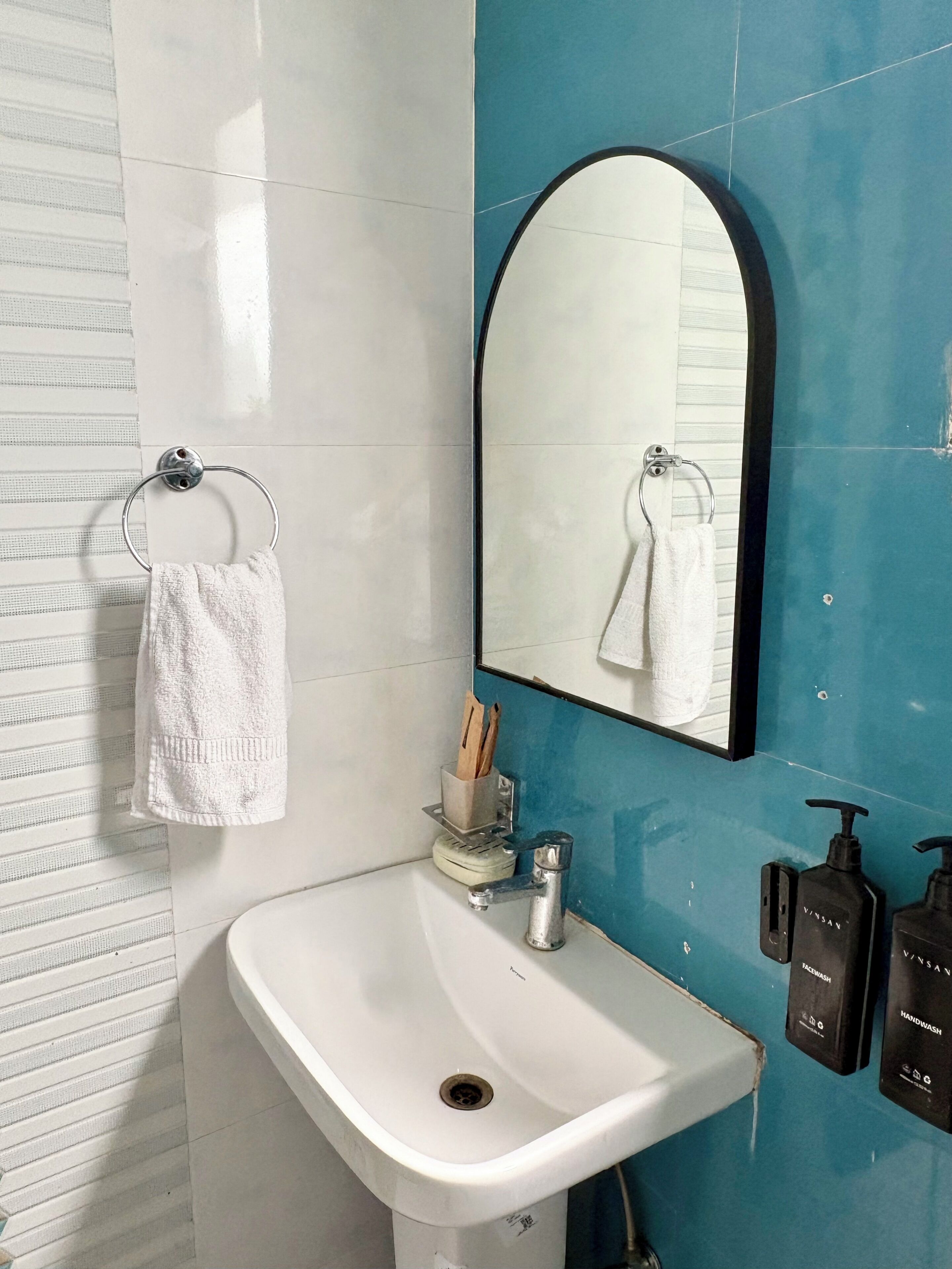 Casa de banho com uma pia branca, um espelho e duas embalagens de gel para as mãos.