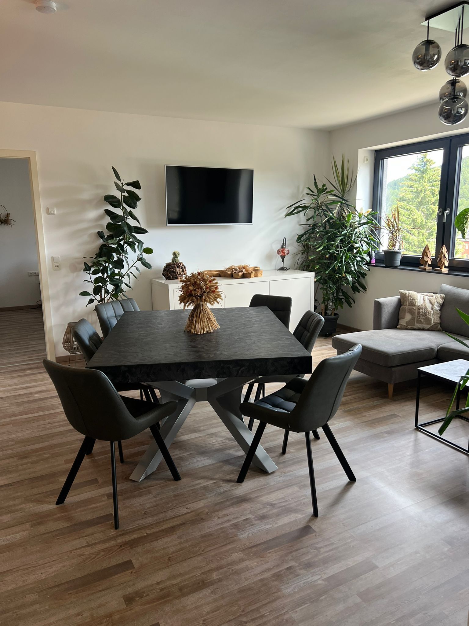 Et moderne spiseområde med et rektangulært bord, seks stole og et fladskærms-tv monteret på væggen.