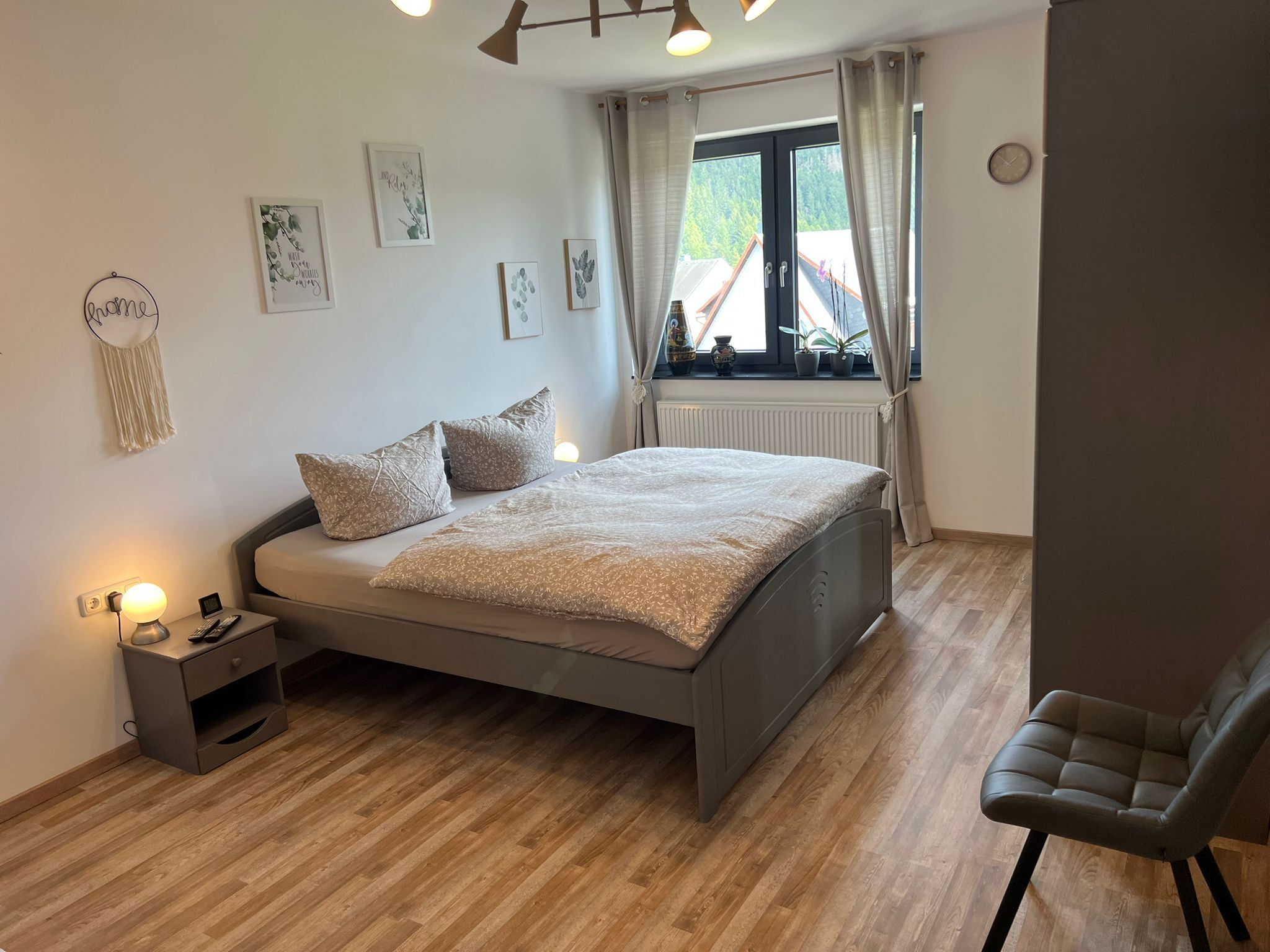 Una camera da letto con un letto, comodino, lampada, sedia e finestra con tende.
