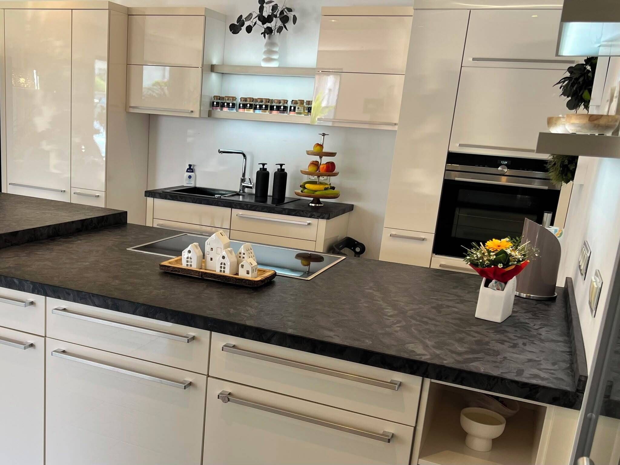 Eine moderne Küche mit schwarzer Arbeitsplatte, weißen Schränken, einem Edelstahlbackofen und einem Spülbecken mit Armatur.