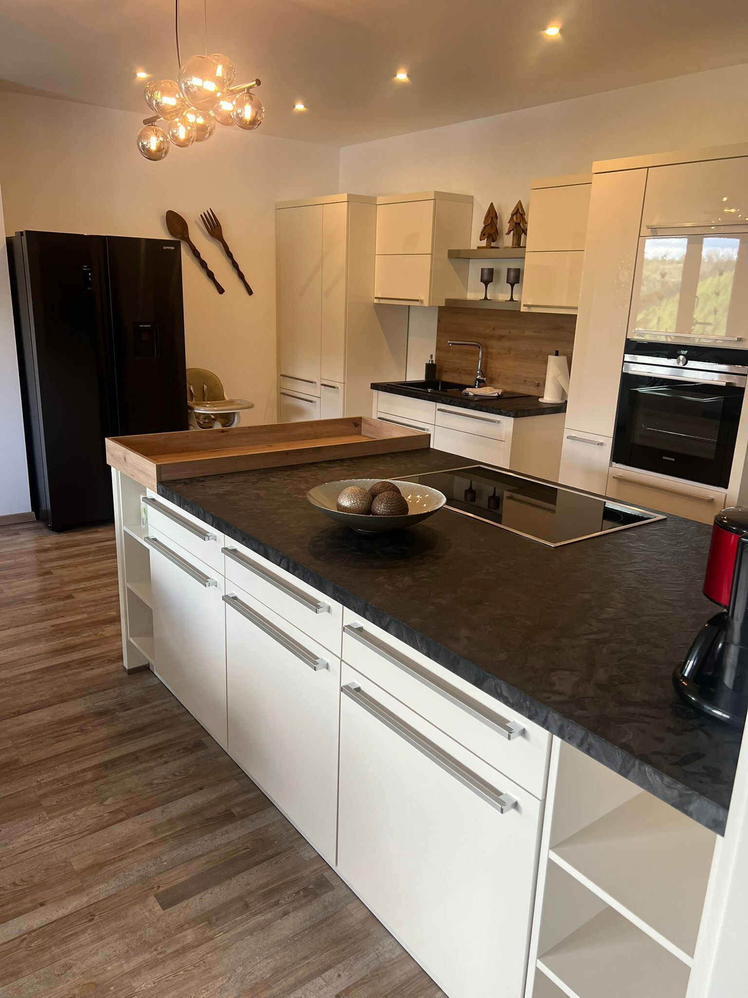 Eine moderne Küche mit einer zentralen Kochinsel, weißen Schränken, einer schwarzen Arbeitsplatte und einem eingebauten Backofen.