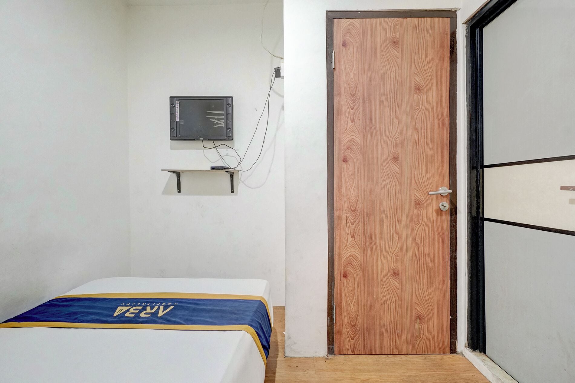 A small room with a bed, a wooden door, a wall-mounted electrical box, and a partial view of a closet.