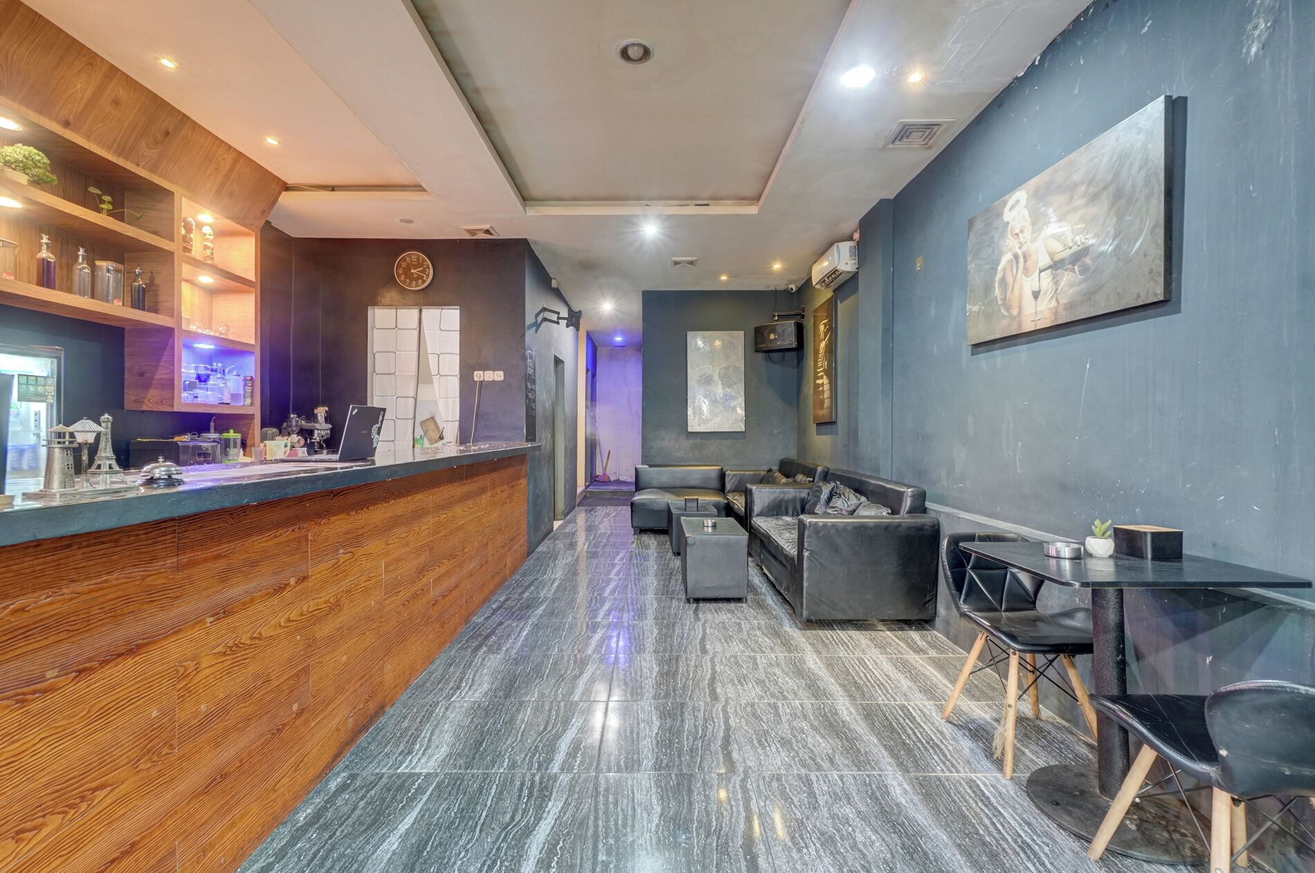 Un área de recepción moderna con mostrador de madera, zona de estar con sofás y sillones, y un cuadro abstracto grande en la pared.