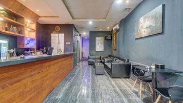 Un área de recepción moderna con mostrador de madera, zona de estar con sofás y sillones, y un cuadro abstracto grande en la pared.