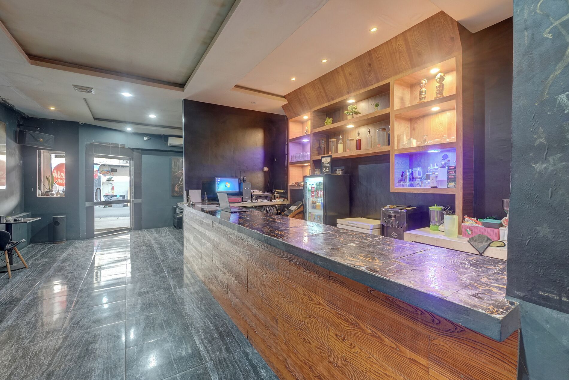 A modern reception area with a marble counter, wooden shelving, and a refrigerator.