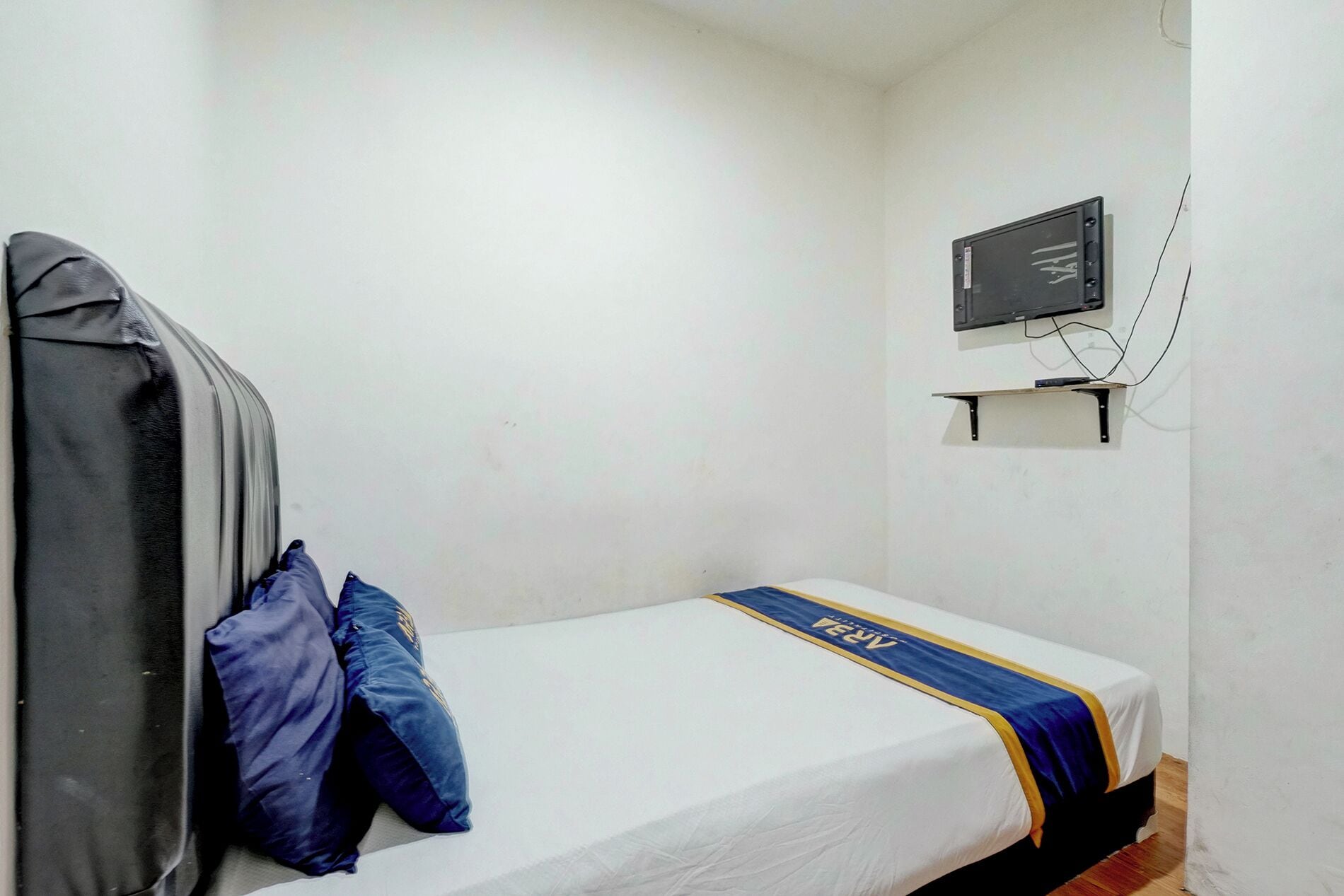 A single bed with a blue and yellow bedspread, a grey headboard, and a wall-mounted television.