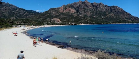 A beach with clear blue water, a sandy shore, and a mountainous backdrop.