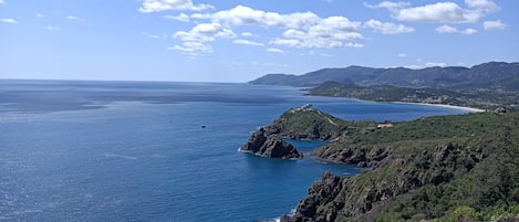 A coastal landscape with a clear sky, rocky terrain, and a view of the sea.
