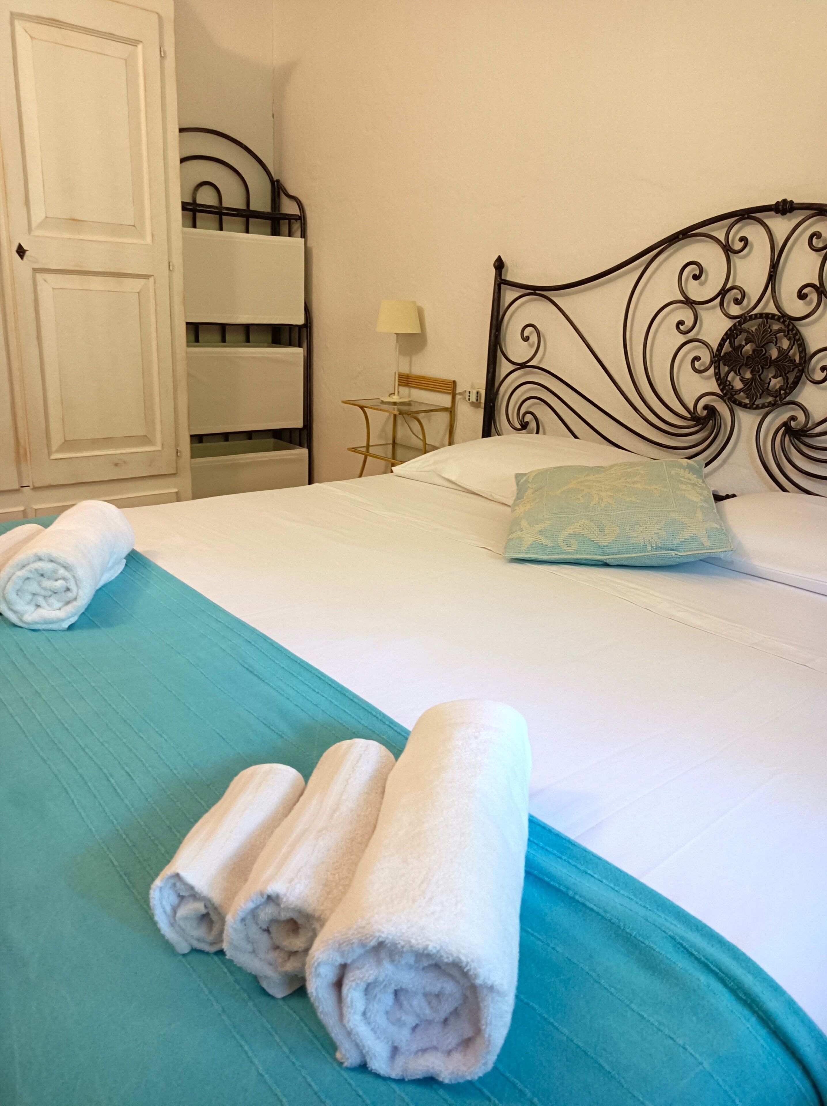 A neatly made bed with rolled towels, a bedside table with a lamp, and a decorative headboard.