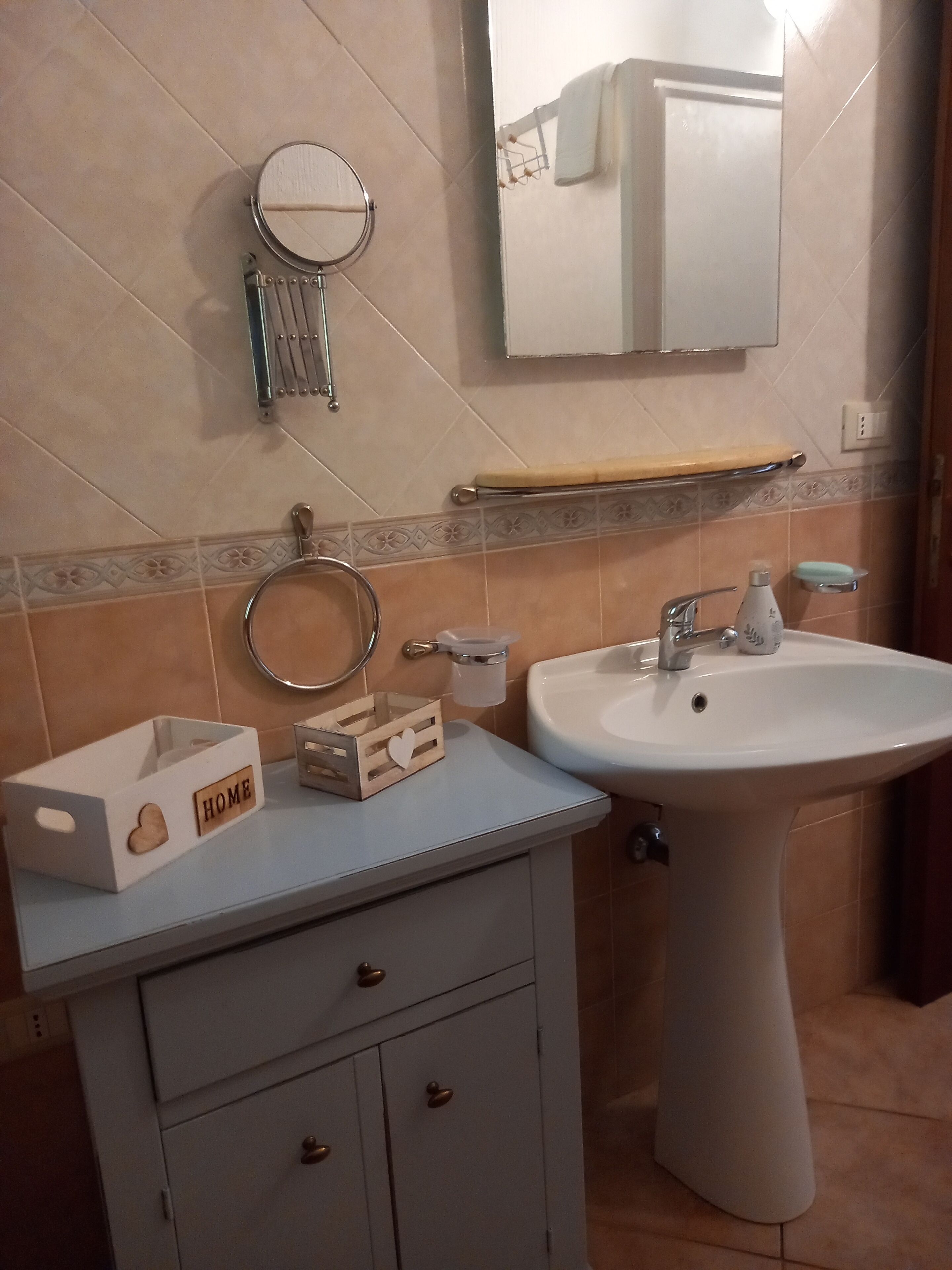 Un baño con lavamanos blanco, un espejo, un inodoro y un armario con cajones.