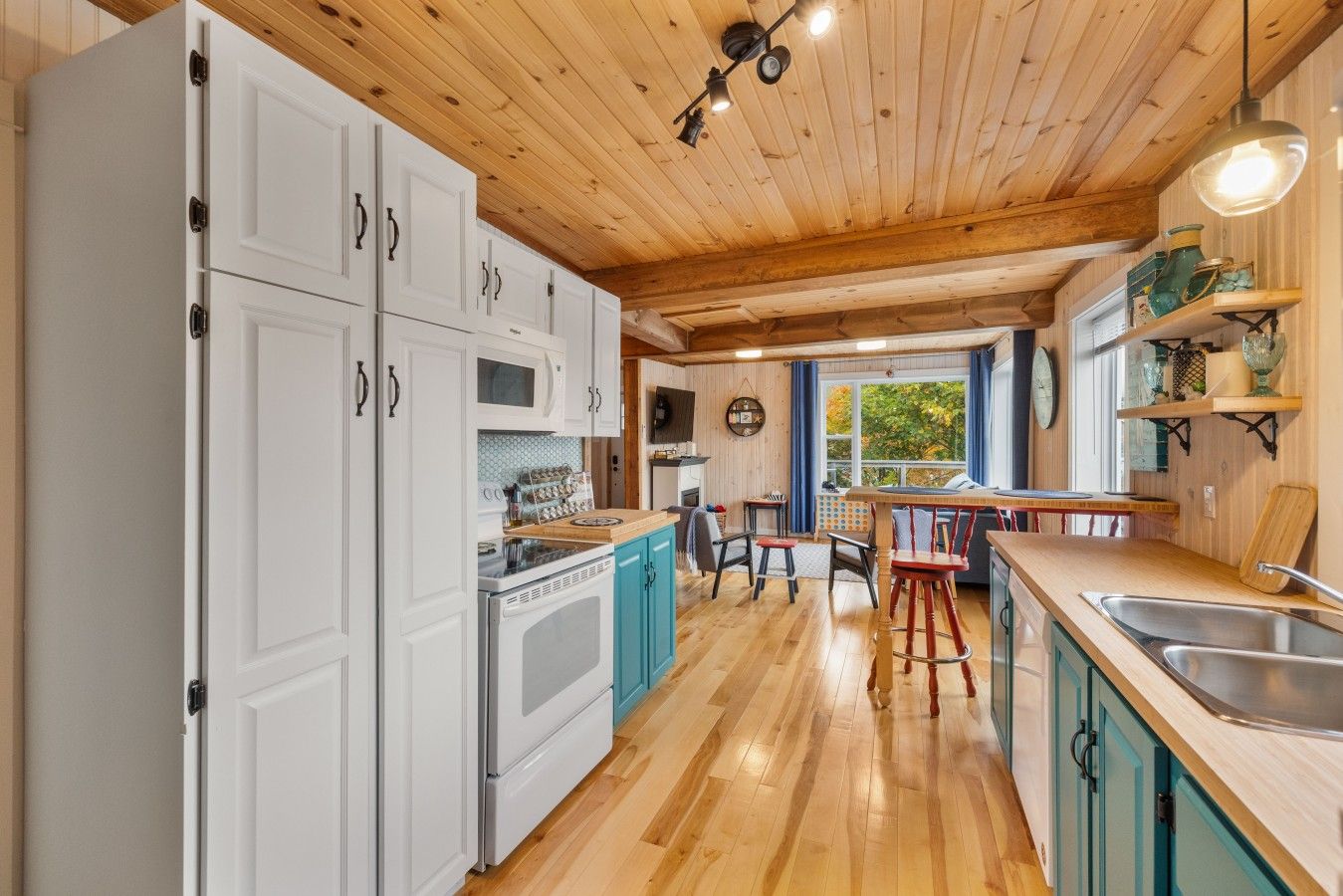 A kitchen with white cabinets, a wooden ceiling, and a window with a view.