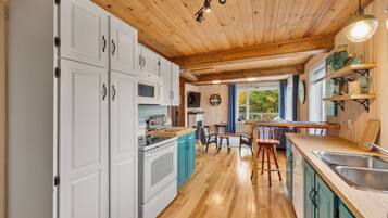A kitchen with white cabinets, a wooden ceiling, and a window with a view.