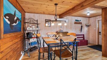 Un interior de madera con una mesa de comedor, sillas, una cafetera y una lámpara colgante.