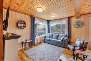 Une pièce chaleureuse avec un plafond en bois, un canapé, une table basse, un téléviseur et une vue sur l’extérieur.