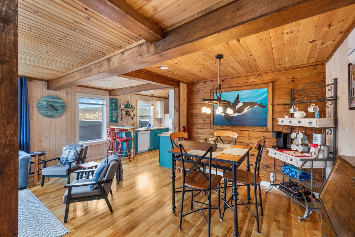 Interior de una cabaña de madera con comedor, cocina y un amplio ventanal con vistas al paisaje.