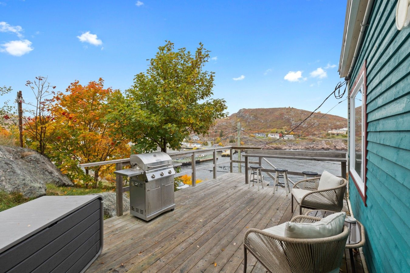 Eine Holzterrasse mit Grill, Gartenmöbeln und Blick auf einen Fluss und Hügel.