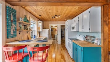 Una cocina con vigas de madera en el techo, armarios blancos, encimera azul y sillas rojas.