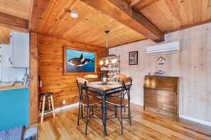 A wooden interior with a dining table, chairs, a kitchen area, and a painting of an orca.