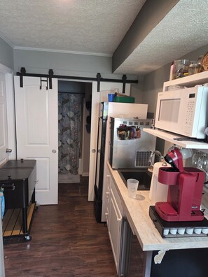 A compact kitchen with a refrigerator, microwave, coffee maker, and a sliding door leading to another room. - Hokie Hideaway - Incredible amenities in an awesome location! (Blacksburg)