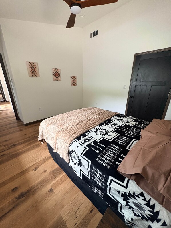 A bedroom with a bed, wooden flooring, a ceiling fan, and a door.