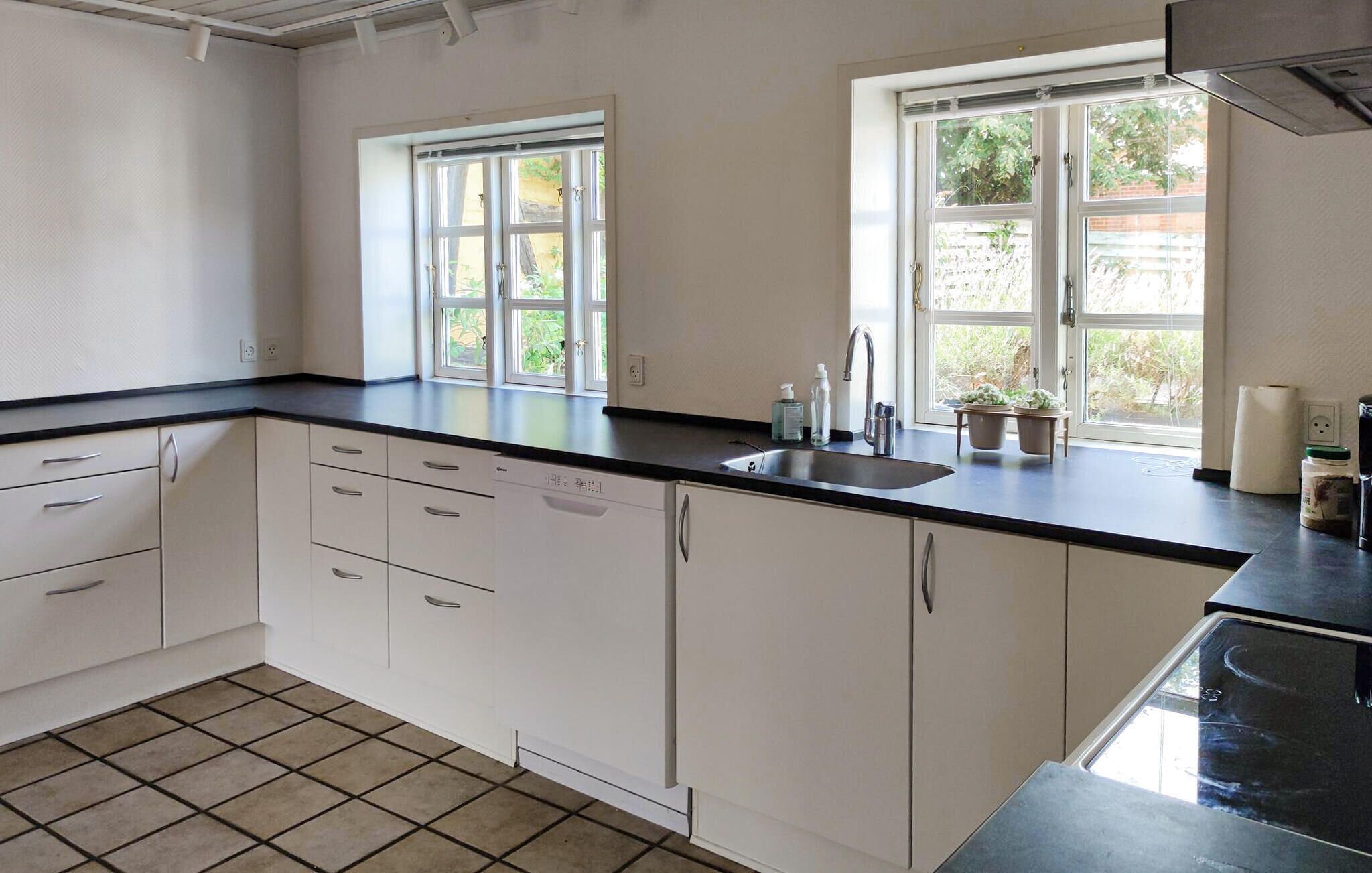 A kitchen with white cabinets, a black countertop, a sink, and two windows providing natural light.