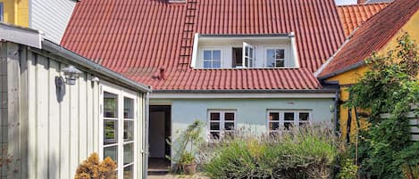 A residential building with a red-tiled roof, a visible window, and a door leading to the entrance.