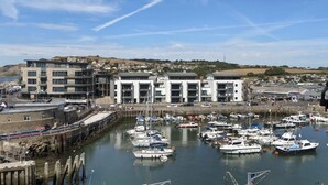 A marina with multiple boats docked, a building with a modern architectural style, and a clear view of the surrounding landscape. - Beautiful Apartment on Pier, Sea Views & Parking (West Bay)