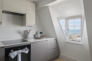 A kitchen with a dishwasher, a window with a view of the sea, and a towel hanging on the oven handle.
