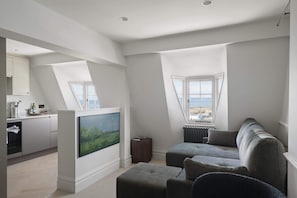 A modern living room with a large window, a flat-screen TV, and a grey sofa.