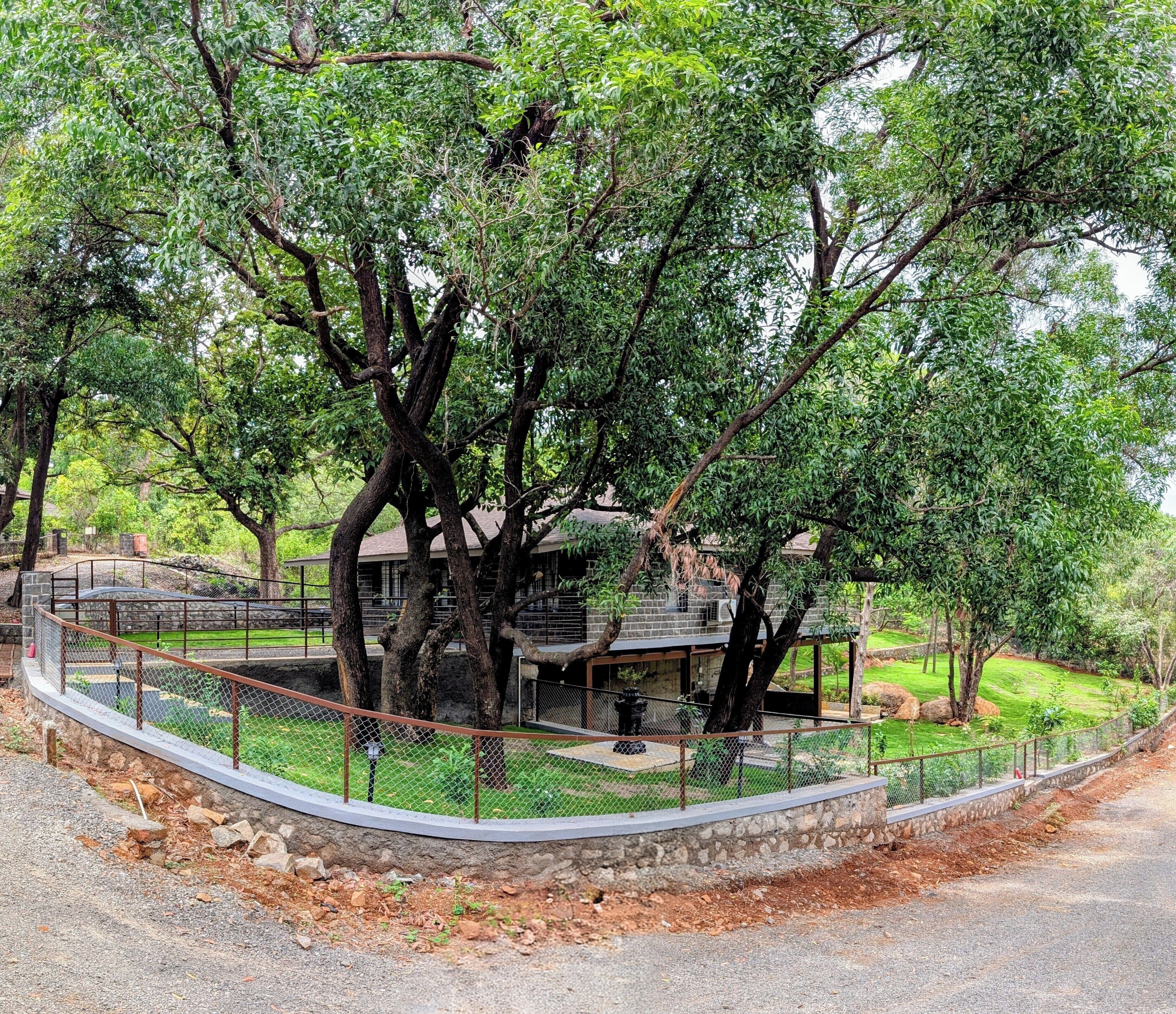 A fenced area with a stone wall and a building with a roof, surrounded by trees.