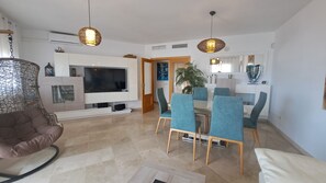 Ein modernes Wohnzimmer mit Fernseher, einer braunen Ledersofa und einem Essbereich mit blauen Stühlen und einem Tisch.