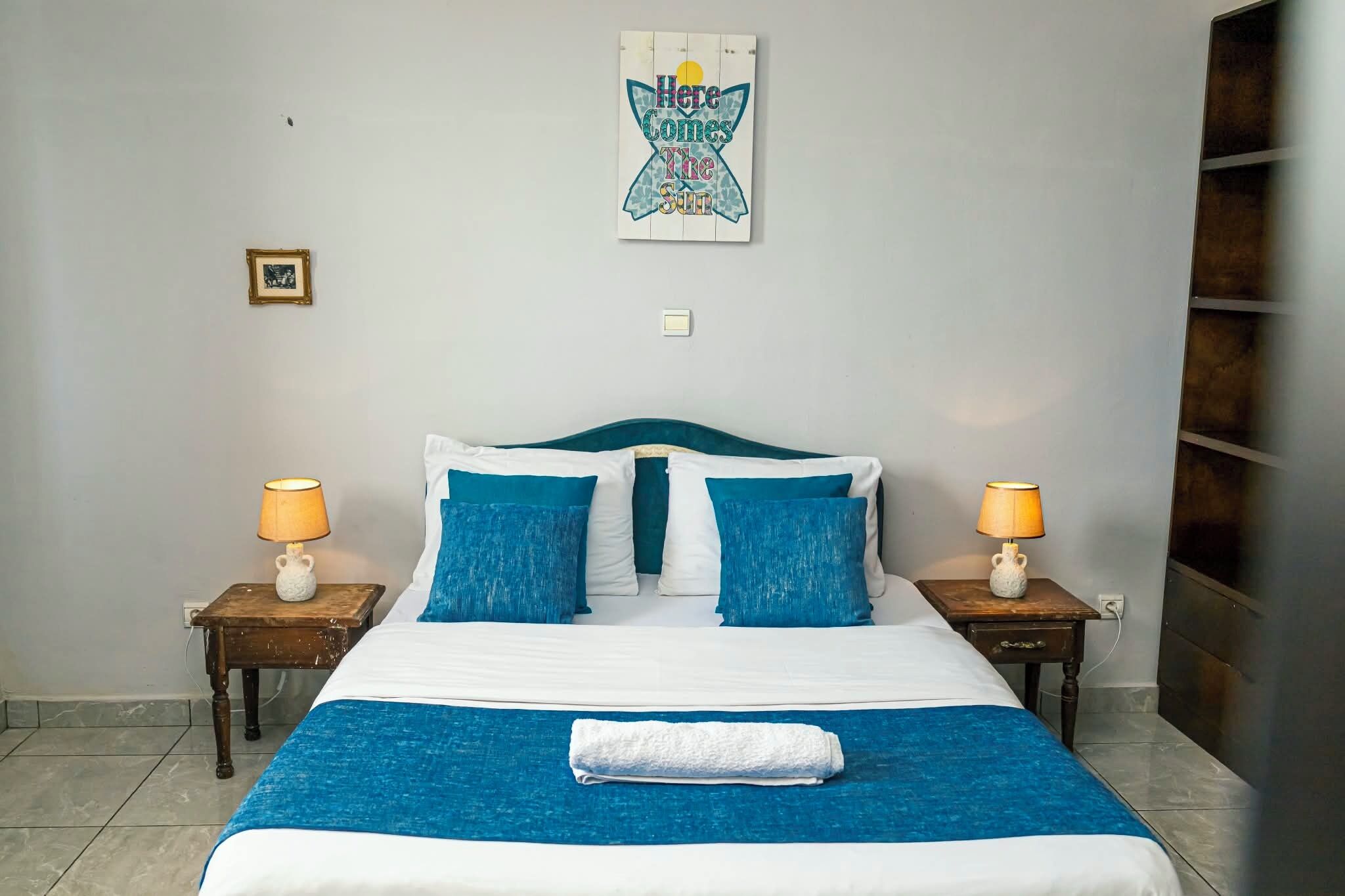 Hotellihuone, jossa on sänky, kaksi yöpöytää, seinäkello ja kehystetty taulu.