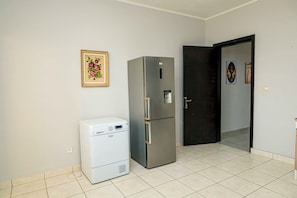 A room with a white air conditioner, a stainless steel refrigerator, and a dark door.