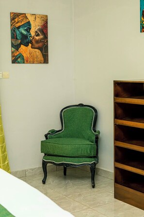 A room with a green upholstered chair, a wooden bookshelf, and a painting on the wall.