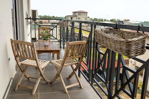 A balcony with a wooden table and chairs, a potted plant, and a wicker basket.