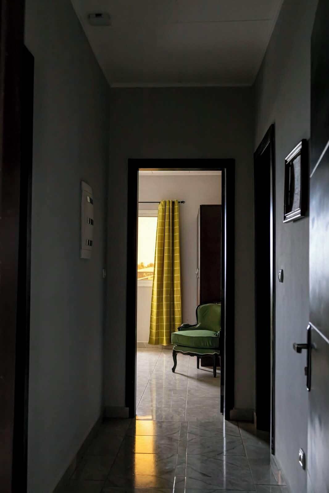 A hallway leading to a room with a green chair and a yellow curtain.