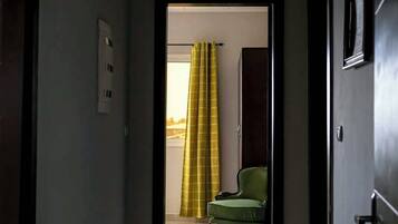 A hallway leading to a room with a green chair and a yellow curtain.