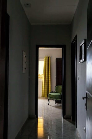 A hallway leading to a room with a green chair and a yellow curtain.