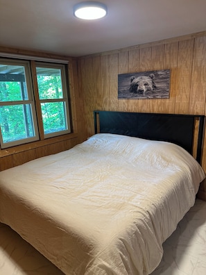 Un dormitorio con una cama, una ventana, paneles de madera y un cuadro de un oso en la pared.
