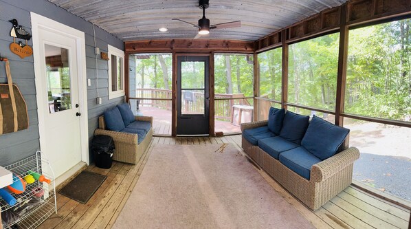 A covered porch with wicker furniture, a ceiling fan, and a view of the outdoors.